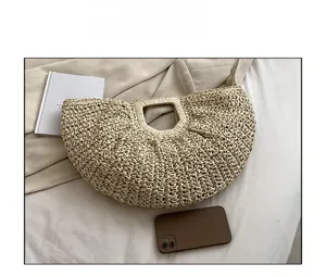 Sizing scale of a semi-circular straw handbag next to a phone for scale reference