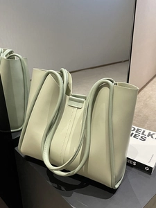 Minimalist light green leather tote bag with unique circular handle and contrast stitching
