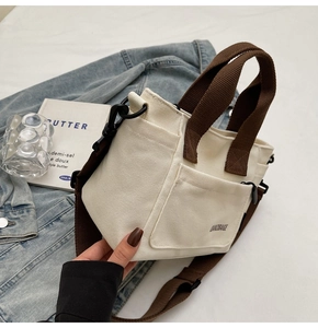 Detail van canvas crossbodytas met bruine handvatten en zwarte afneembare schouderriem