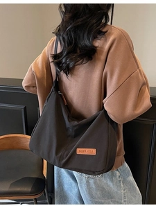 Minimalist black nylon tote bag with leather logo patch shown in a lifestyle shoulder view