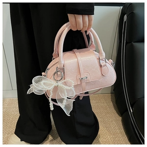 Pink shell bag with elegant white organza bow and pearl charm detail shown held by hand