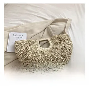 Detail view of a crescent handmade woven straw bag with circular handle on white linen