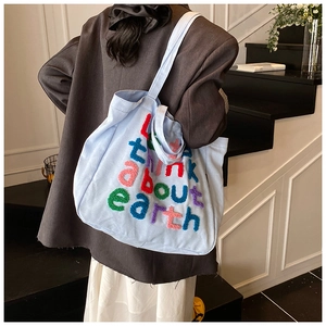 Bolso tote de lona azul con bordado colorido llevado al hombro por una modelo