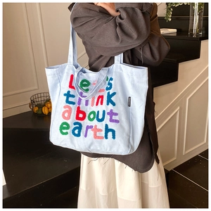 Detalle del bolso tote de lona azul claro con bordado de letras coloridas en la correa