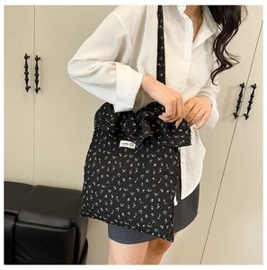 Détail du sac cabas floral noir à volants porté à l'épaule sur un modèle féminin
