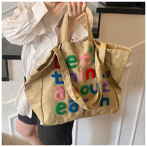 Primer plano de bolso tote de lona beige con letras coloridas bordadas de estilo ecológico