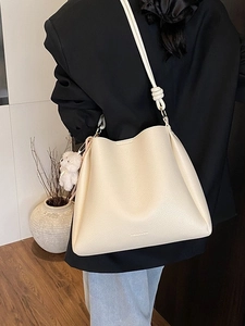 Sac seau beige chic avec texture litchi et charmant ours, porté à l'épaule pour femme