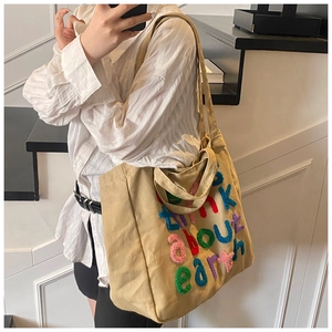 Detalle del bordado colorido 'think about earth' en el bolso de lona beige para mujer