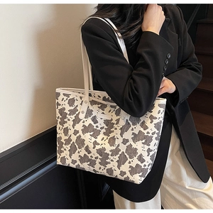 Detail van grote tote bag met koeprint gedragen bij zwarte blazer en witte pantalon