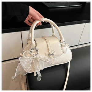 Detailed close-up of cream shell bag with pearl-luster texture and bow charm