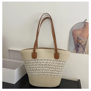 Detail of woven straw tote bag featuring intricate openwork patterns and brown leather handles