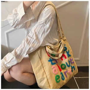Detalle del bolso tote de lona beige con bordado colorido del texto Think About Earth