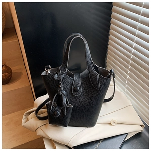 Close-up of black lychee grain leather bucket bag set on beige fabric with metal buckles