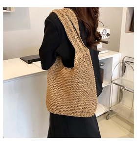 Dettaglio della grande borsa tote in paglia intrecciata indossata a spalla da una modella