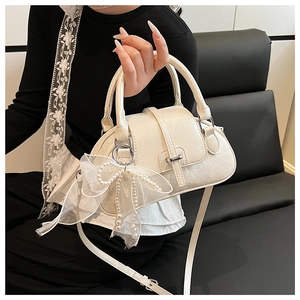 Detail of cream bow shell bag with lace pearl pendant and glossy patent texture