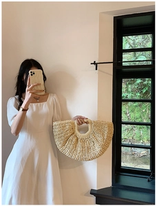 Detail of the woven texture and reinforced handle on a beige straw crescent handbag