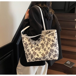 Detail van grote shopper met koeienprint getoond met zwart pak op houten trappen
