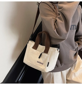 Detail van beige canvas tas met bruine banden en tekstlogo op de zijkant