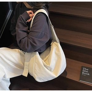 Close-up of cream canvas crescent tote bag with wide strap on a wooden staircase