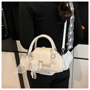 Detail of elegant cream shell handbag with delicate lace bow and pearl charm accessory
