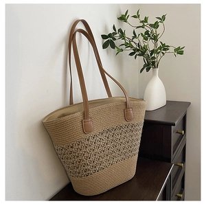 Straw tote bag with brown leather handles and hollow woven pattern against a minimalist wall