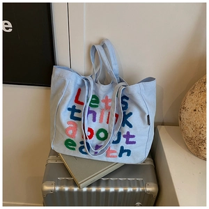 Detalle del bolso tote de lona azul claro con bordado colorido sobre maleta plateada