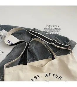 Détail de la bandoulière noire réglable avec boucle en métal sur le sac cabas en toile