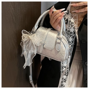 Close-up of silver shell bag with pearl bow charm and mesh detail held by hand
