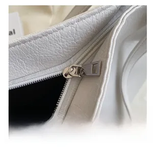 Detailed close-up of smooth metal zipper and white pebbled leather texture on tote bag