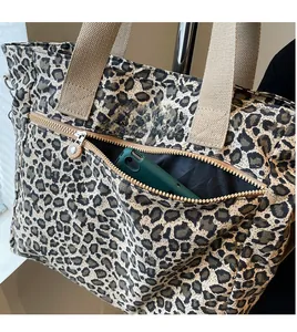 Detail of the leopard print tote bag showing a front zipper pocket holding a smartphone