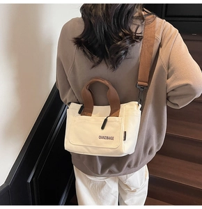 Detail van de crème canvas crossbodytas met bruine handvatten en geborduurde zak