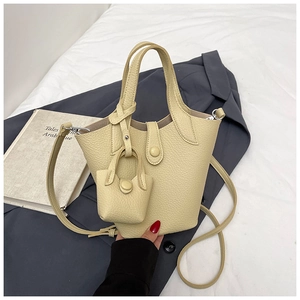 Detail of beige litchi grain leather bucket bag with mini charm and strap on soft blazer