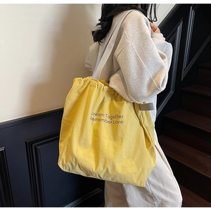 Detail of yellow canvas tote bag featuring purple lettering and drawstring closure