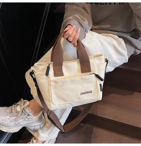 Detail van de crèmekleurige canvas tas met bruine handvatten en merklogo-opdruk