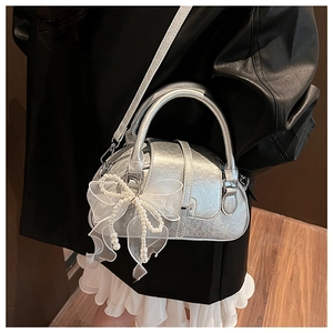 Detail of silver metallic shell bag with mesh bow and pearl charms worn by a model