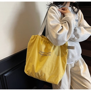 Detail of yellow canvas tote bag featuring drawstring pleats and printed slogans
