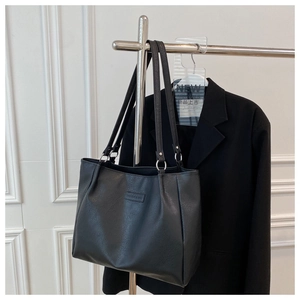 Detail of matte black PU leather tote bag featuring silver metal rings and brand patch