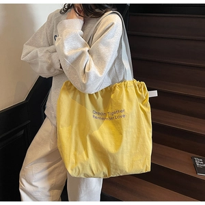 Close-up of yellow drawstring tote bag with Dream Together Remember Love purple text