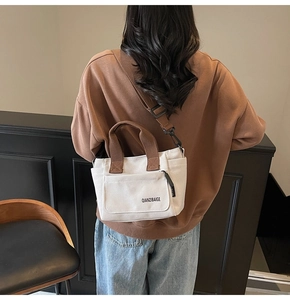 Detail van canvas crossbodytas met contrasterende banden en voorvak met merknaam