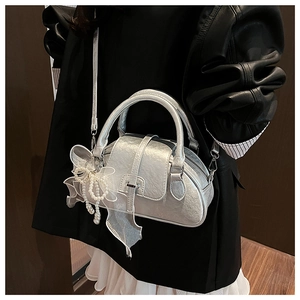 Macro detail of silver metallic shell bag featuring pearl bead and organza bow charm