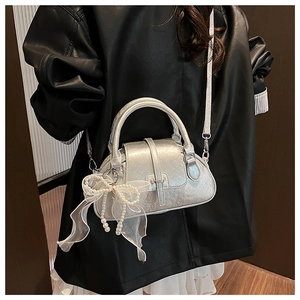 Silver metallic shell bag with pearl bow charm worn as a stylish crossbody bag