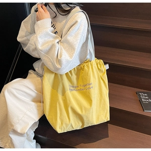 Detail of yellow canvas drawstring tote bag featuring purple slogan on a casual model