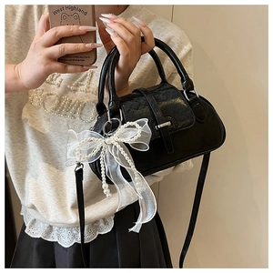 Detail of black glossy shell bag featuring white organza bow and elegant pearl chain
