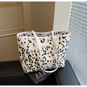 Detailopname van de tote bag met koeprint, logo en zilveren klinknagels aan de riem