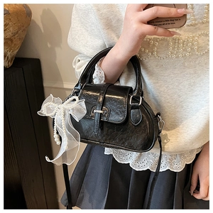 Detail shot of black textured PU leather bag with white pearl ribbon bow charm