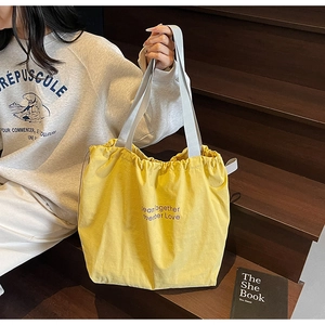 Detail of yellow canvas drawstring tote bag with purple typography and grey webbing straps