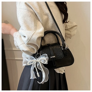 Detail of retro black shell bag featuring white lace pearl bow and stylish handle