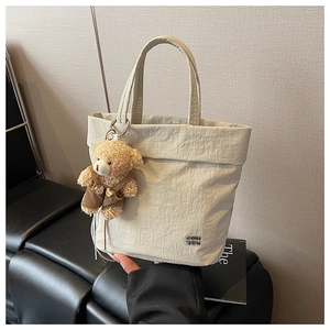 Detail of off-white textured canvas tote bag with a cute brown bear plush charm