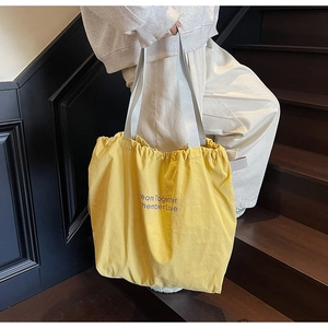 Detail of yellow canvas tote bag with purple lettering and white shoulder strap on stairs