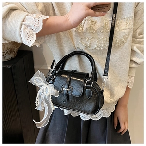 Close-up of black crossbody shell bag with white lace bow and pearl charm detail